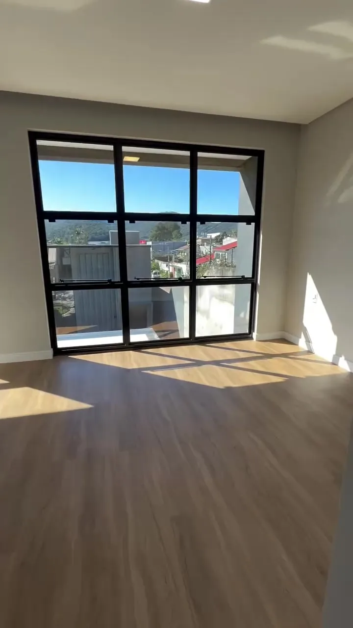 Sala vazia com grande janela de esquadria preta e vista para o entorno