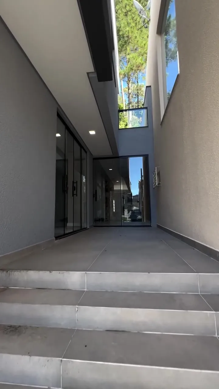 Acesso lateral de residência com pé direito alto, portas de vidro e paredes cinza